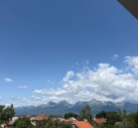 View from Hurbanova Street in Poprad towards the Tatras, with red roofs and a blue sky.