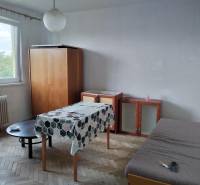A room in a 2-room apartment with a wooden floor, a table, and a wardrobe.