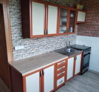 A kitchen in a 2-room apartment with cabinets and equipment, brick wall appearance.