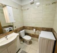 Bathroom with a washing machine and toilet in a 2-room apartment, light tiles.