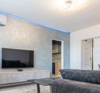 Living room in a three-room apartment with a gray sofa and a TV on the wall.