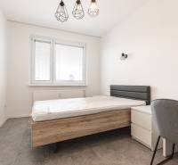A bedroom with a gray bed and chair in a three-room apartment.