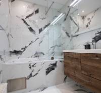 A bathroom with a marble wall, a bathtub, and a wooden cabinet in a 3-room apartment.