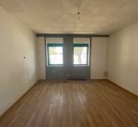 A room with a wooden floor and two windows as part of apartment construction.