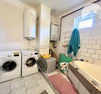 A bathroom in a family house with a washing machine, dryer, bathtub, and boiler.