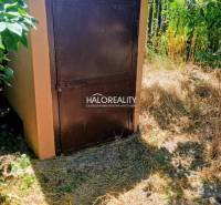 A small, brown-orange structure with metal doors in the garden setting of a family house in Váhovce.