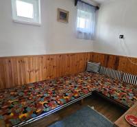 A room in a family house with wooden paneling, colorful mattresses, a small window, a lamp.