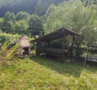A garden gazebo and a fireplace by the cottage in Ružín, Malá Lodina, surrounded by wooded hills.