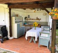 In the summer kitchen of a family house in Pányok, there is a terrace with a table, chairs, a grill, and flowers.
