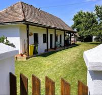 A family house in Pányok with a lawn, flowers on the terrace, a wooden fence, trees in the yard.