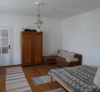A room in a family house with a chandelier, a couch, a bed, and a wooden floor.