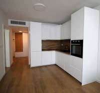 A kitchen in a 2-room apartment with white cabinets and wooden flooring.