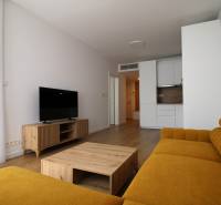 Living room of a two-room apartment, wooden furniture, yellow sofa, television, kitchen unit in the background.