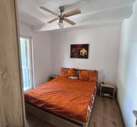 Bedroom in a 2-room apartment with a double bed, ceiling fan, and table.