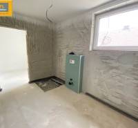 A room under construction with a window, the floor is concrete, the room will be in a 5 or more room apartment.