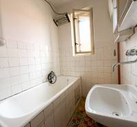 A bathroom in a family house with an older bathtub, a sink, and a window.