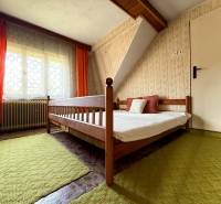 A bedroom in a family house with a wooden bed, orange curtains, and a green carpet.
