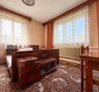 A room in a family house with carpets, windows with curtains, and wooden furniture.