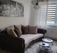 A comfortable couch with cushions and a painting in a studio apartment, next to coffee tables.