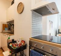 A kitchen with a cooktop and a range hood in a two-room apartment, complemented by a clock and kitchen utensils.