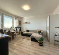 A bright living room in a two-room apartment with a sofa, dining table, and large windows.