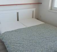 A bedroom with a double bed, white furniture, and two wall shelves in a two-room apartment.