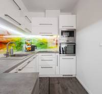 A kitchen in a 2-room apartment with a colored glass backsplash and built-in appliances.