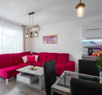Living room in a two-room apartment with a red sofa, glass table, and flowers.