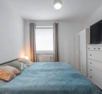 Bedroom in a 2-room apartment with a light bed, wardrobe, and a TV on a dresser.