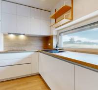 The kitchen of a 3-room apartment with white cabinets, a wooden countertop, and appliances.