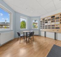 A room in a family house with windows, a table, and chairs by the wall with frames.