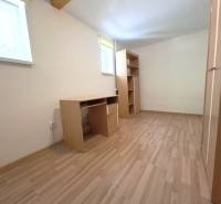 A room in a 4-room apartment with wooden flooring, a writing desk, and shelves.