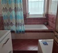 A bathroom in a 4-room apartment with a bathtub, curtain, washing machine, and window.