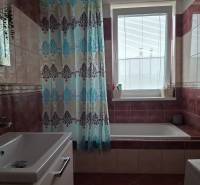 A bathroom with a curtain and a bathtub, tiles in brown shades, a bright window, a 4-room apartment.