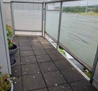 A small balcony in a 4-room apartment with flower pots and a matte railing.