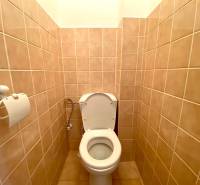 A toilet in a 2-room apartment with beige tiles and a toilet paper holder.