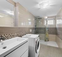Bathroom with a washing machine, shower, and sink, on Pluhova Street in a family house, light tiles.