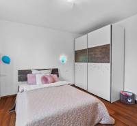 Bedroom with a bed, wardrobe, and lamp, Pluhová, in a family house with wooden flooring.