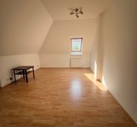 Room with a slanted ceiling, wooden decor floor, table, well-lit.
