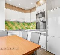 A kitchen in a 3-room apartment with colorful tiles, a white refrigerator, and a wooden table.