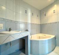 A bathroom with a corner bathtub and a sink in a 3-room apartment, tiled with light blue tiles.