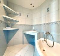 A bathroom in a 3-room apartment with a corner bathtub and wall shelves.