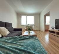 Living room with a gray sofa, television, and wooden floor in a three-room apartment.