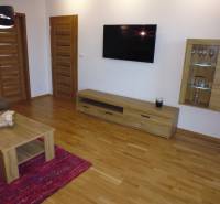 Living room in a 3-room apartment with wooden flooring, furniture, and a TV on the wall.