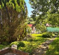 A garden in Mojš with a cottage surrounded by greenery and fruit trees.