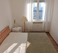 A bedroom with a bed, a lamp, and a table in a two-room apartment, large window.