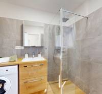 Bathroom with a shower, washing machine, and wooden cabinet in a 3-room apartment.