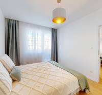 A bedroom with a bed and a view of the living room in a 3-room apartment.