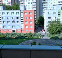 A view of colorful apartment buildings, greenery, and a parking lot from a 3-room apartment.