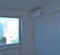 A room in a 3-room apartment with a window and air conditioning, view of apartment blocks.